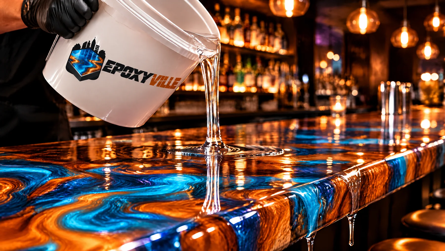 Clear epoxy pouring from a Epoxyville bucket onto a metallic bartop